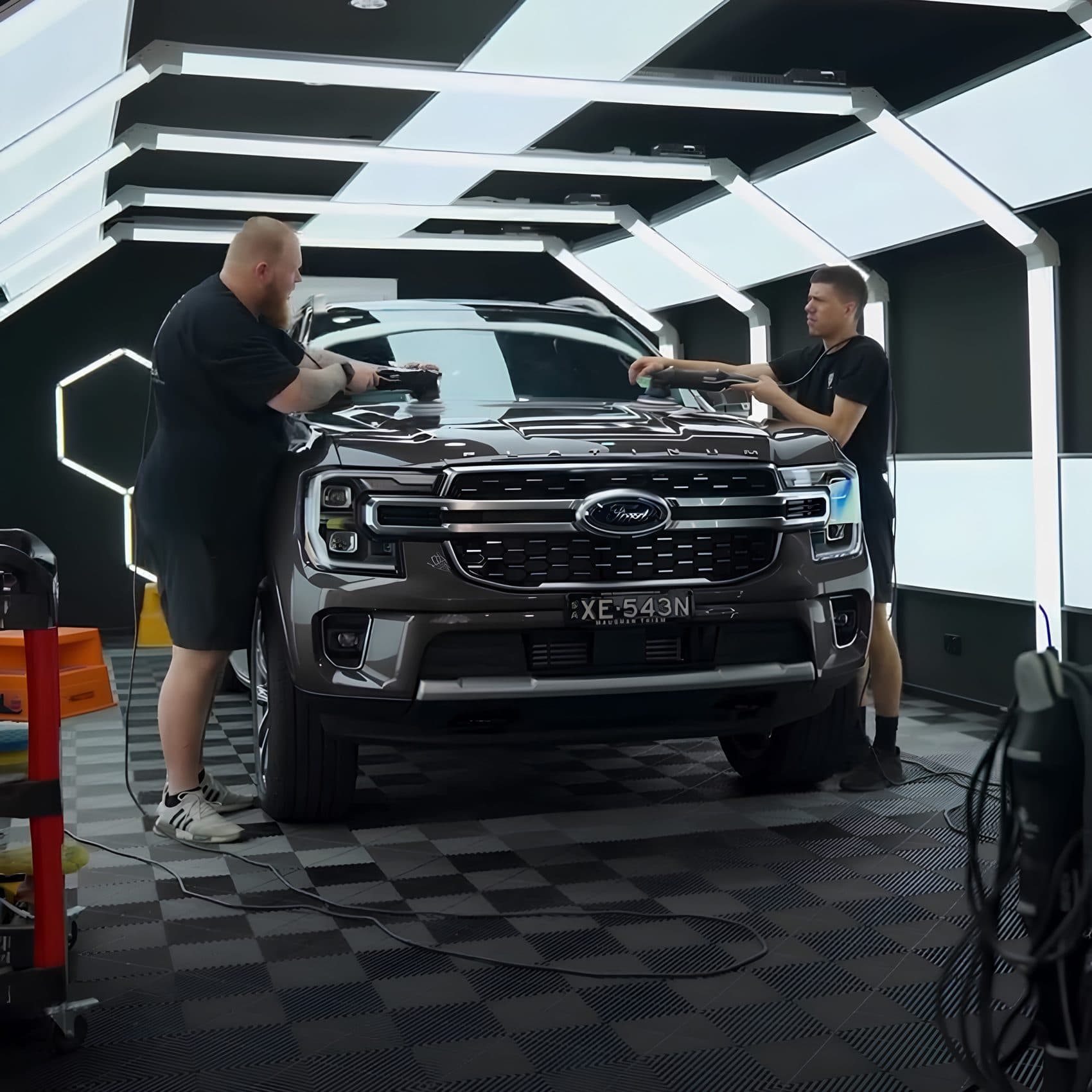 Two detailers machine polishing the bonnet of a Ford SUV