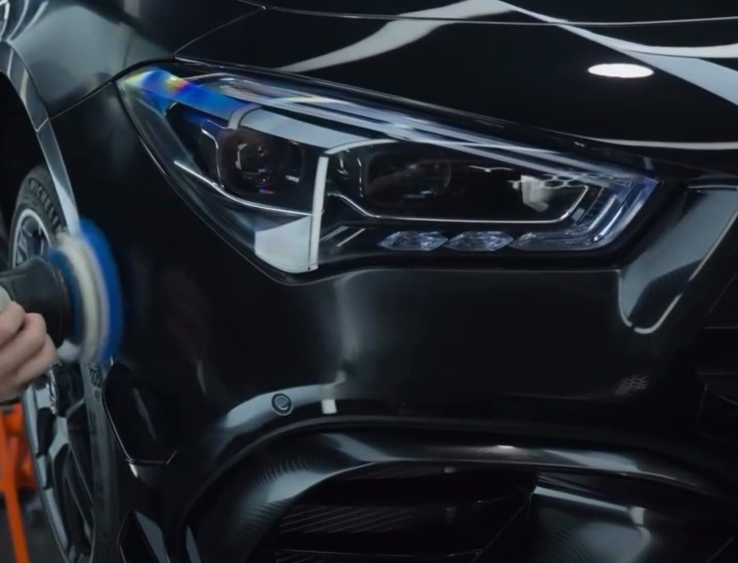 Machine polisher working alongside the clear headlight of a black Mercedes AMG